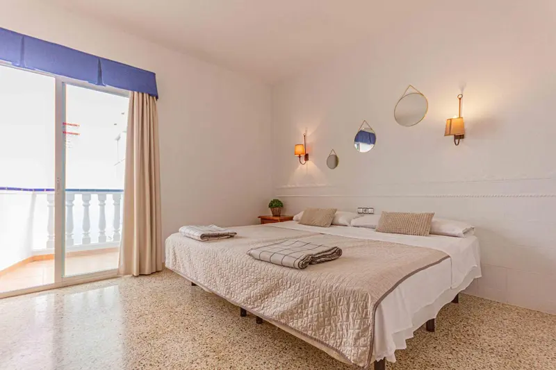 Chambre lumineuse avec un grand lit et un accès à un balcon.