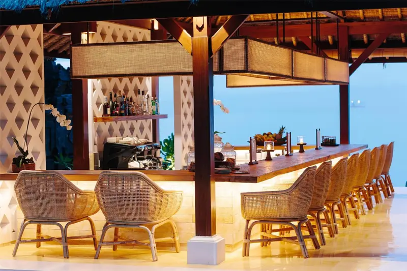 Un bar en plein air avec des tabourets et des fauteuils, donnant sur la mer.