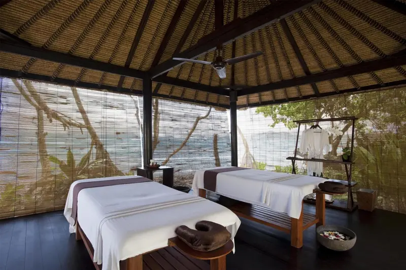 Espace de massage en plein air avec deux tables de soins face à la mer.