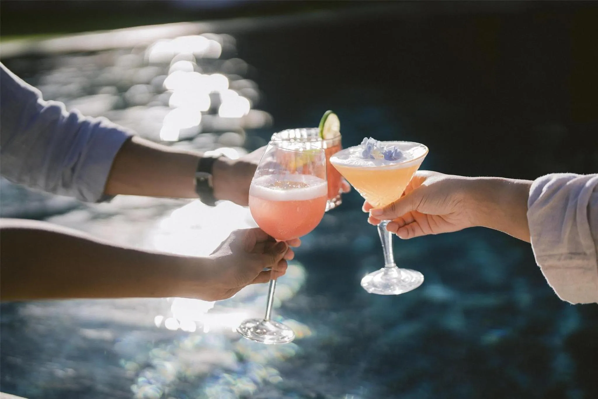 Deux personnes trinquent avec des cocktails colorés au bord d'une piscine.