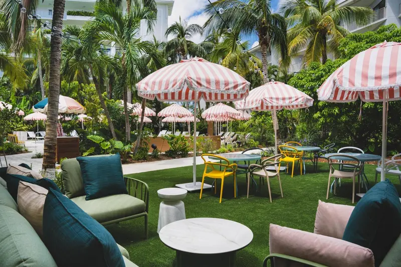 Espace extérieur aménagé avec des parasols rayés, des tables et des fauteuils colorés sur une pelouse artificielle.