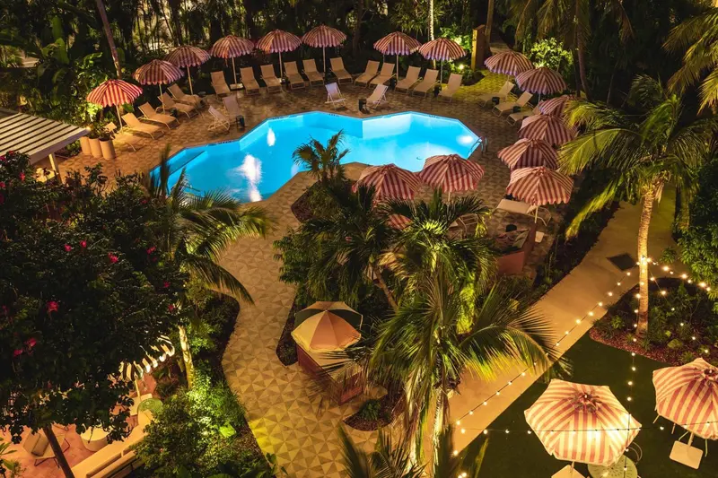Vue aérienne d'une piscine illuminée entourée de transats et de parasols.