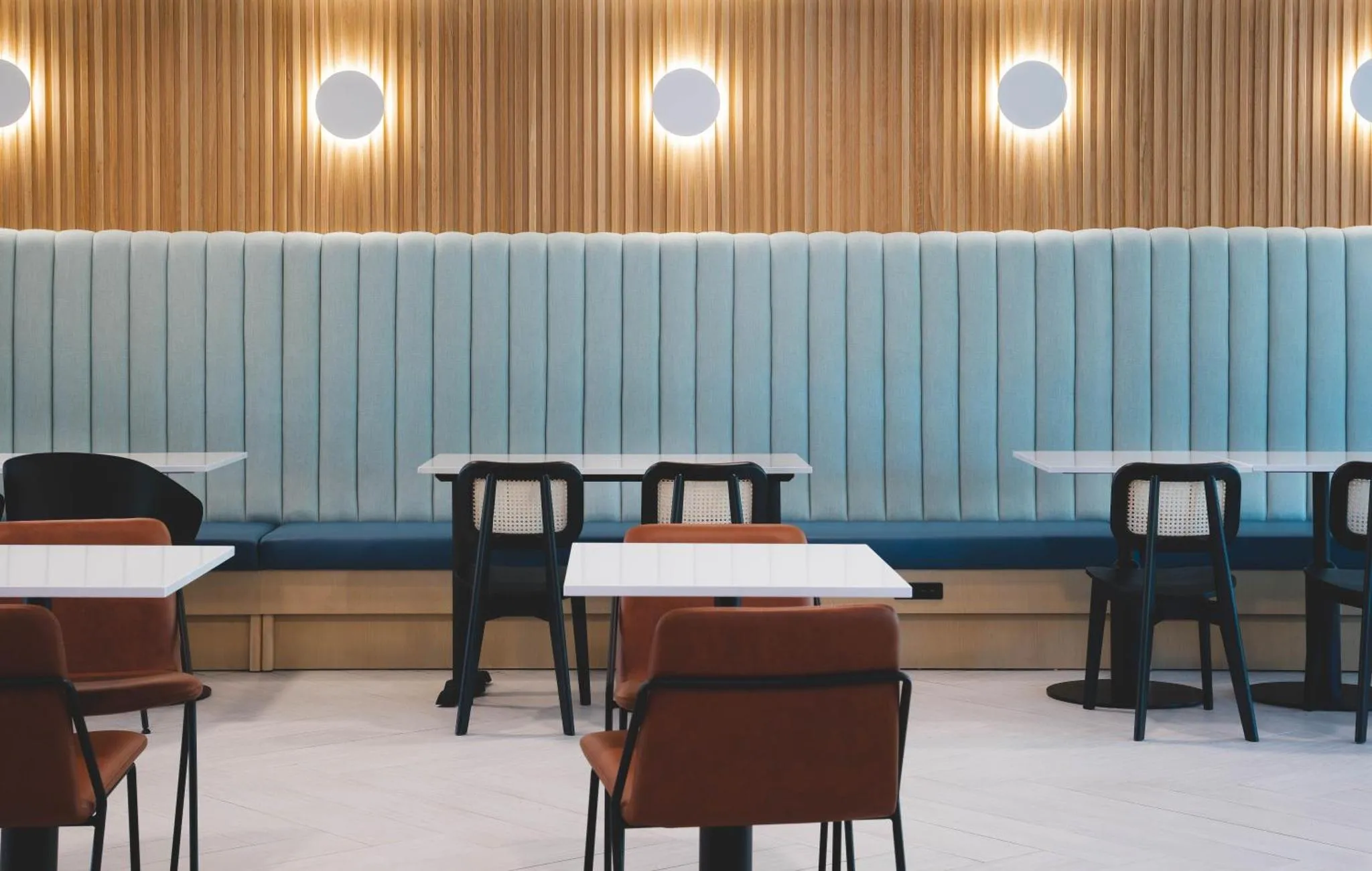 Une salle de restaurant lumineuse avec des banquettes bleues et des tables blanches.