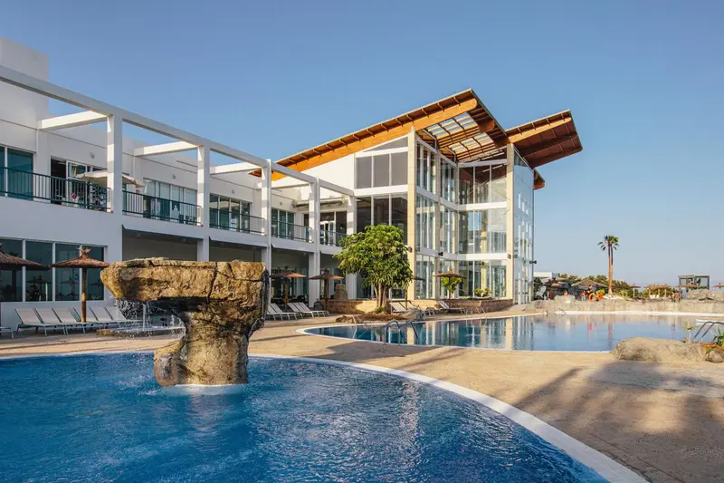 Bâtiment moderne blanc avec piscine et fontaine en pierre.