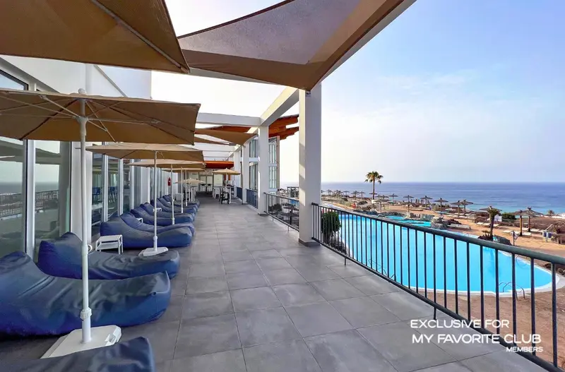 Terrasse avec transats et vue sur la mer et une piscine.