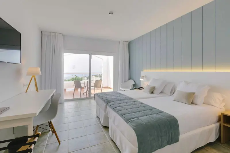 Chambre lumineuse avec un grand lit et une vue sur la mer.