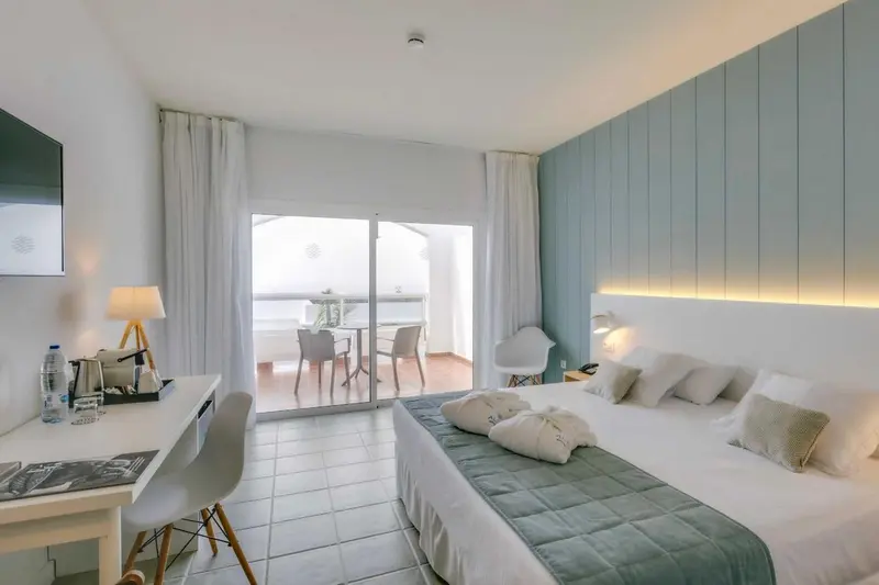 Chambre lumineuse avec un lit double et un accès à un balcon.