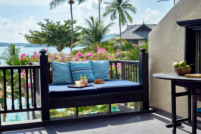 Terrasse avec assise et table basse donnant sur une végétation luxuriante et la mer.