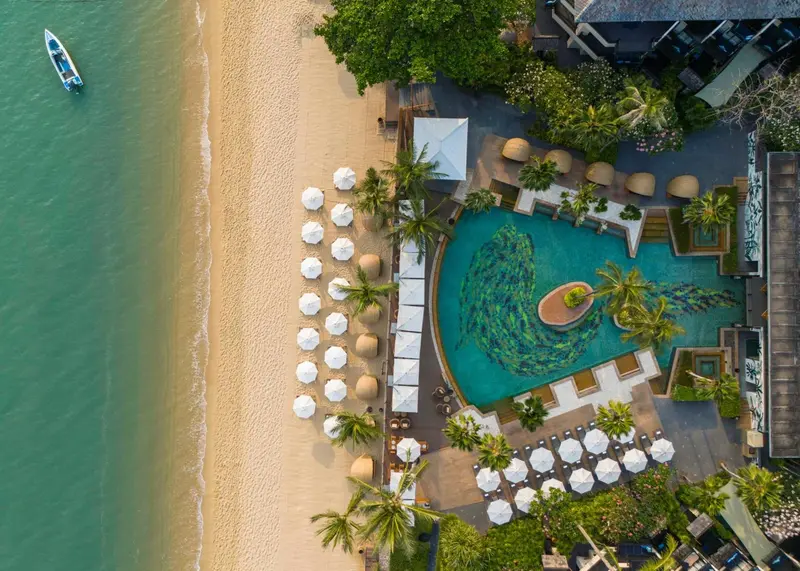 Vue aérienne d'une plage bordée de transats et d'une piscine sinueuse.