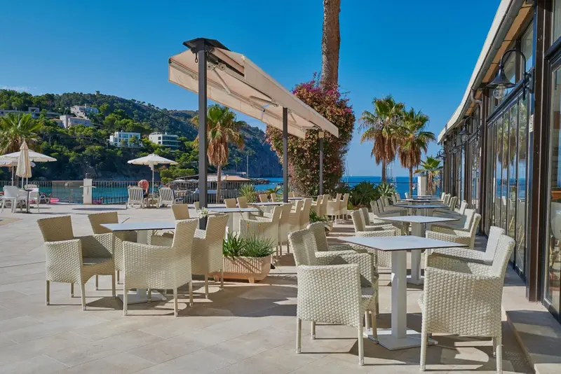 Terrasse ombragée avec tables et chaises en osier donnant sur la mer.