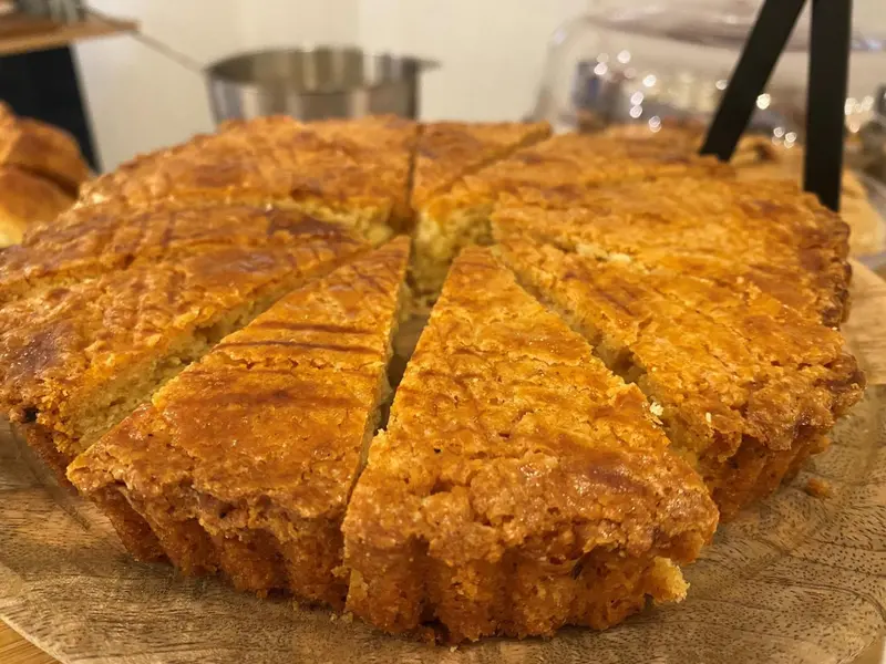 Une tarte aux pommes dorée, coupée en parts, est présentée sur un plateau en bois.