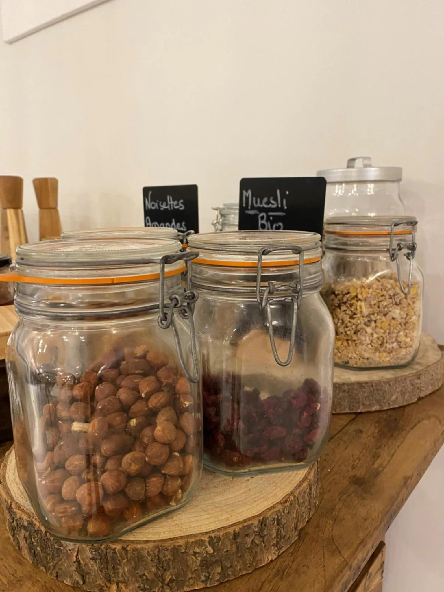 Des pots en verre remplis de céréales et de fruits secs sont posés sur une planche en bois.