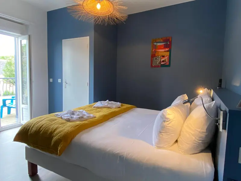 Une chambre lumineuse avec un grand lit recouvert d'une couverture jaune et de coussins blancs.