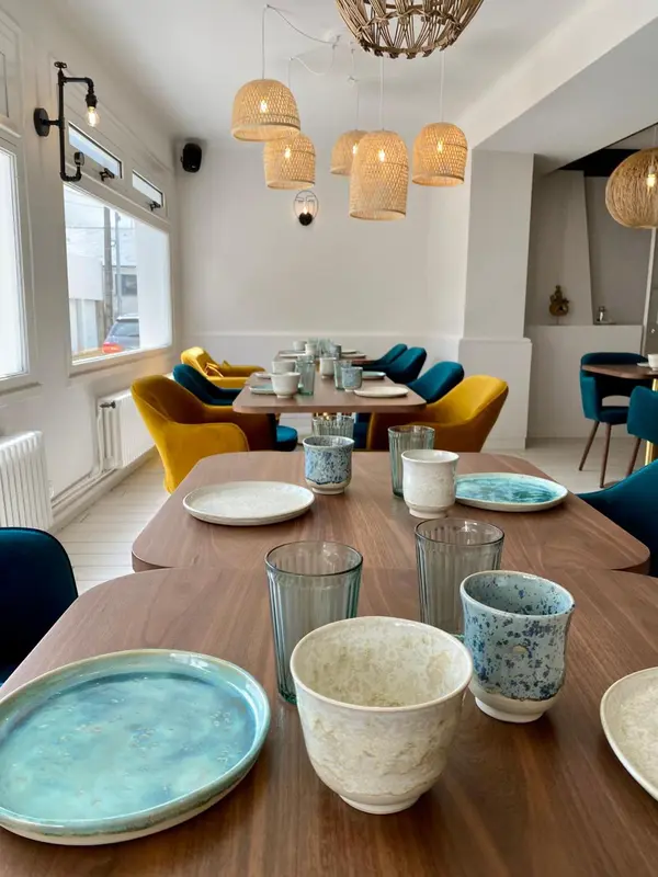 Une table en bois est dressée avec de la vaisselle colorée dans une salle lumineuse.