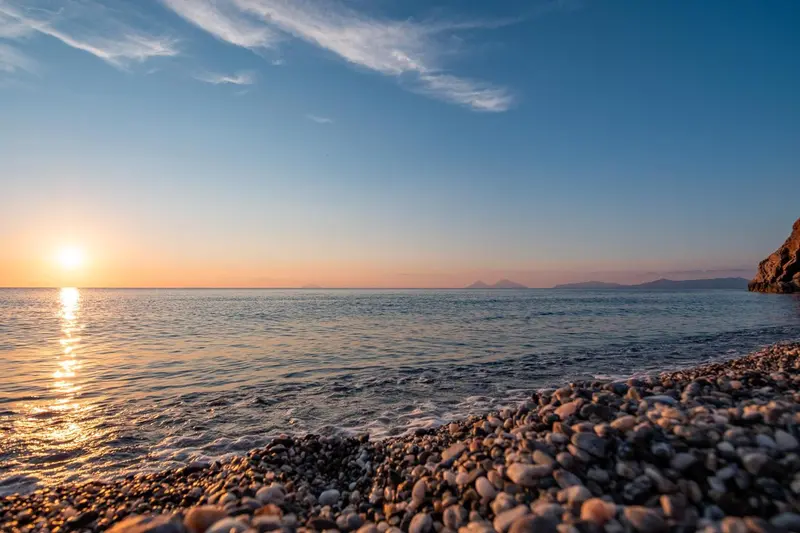 Coucher de soleil sur une plage de galets avec une mer calme.