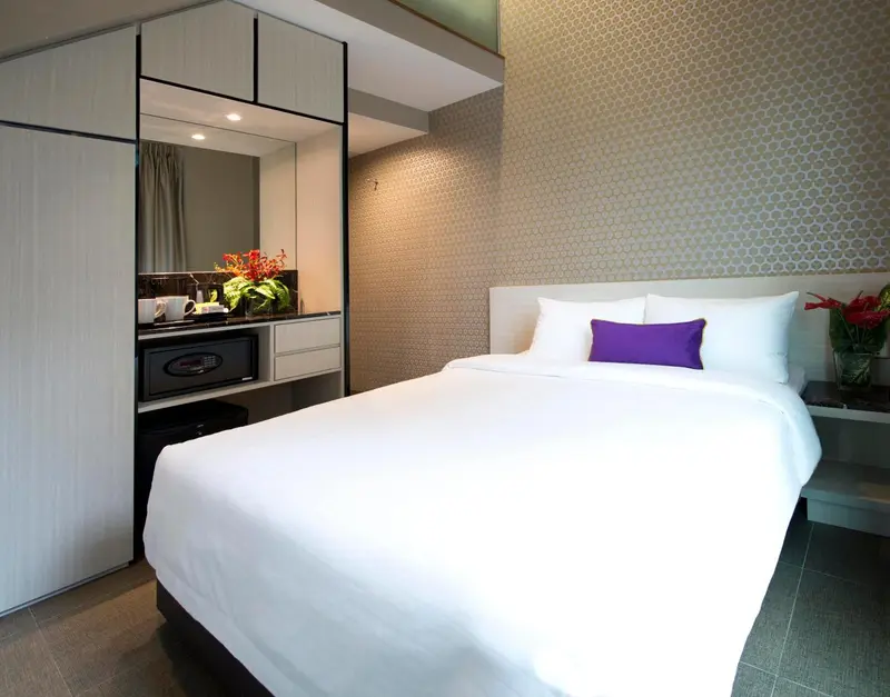 Une chambre lumineuse avec un grand lit recouvert de draps blancs et des oreillers violets.