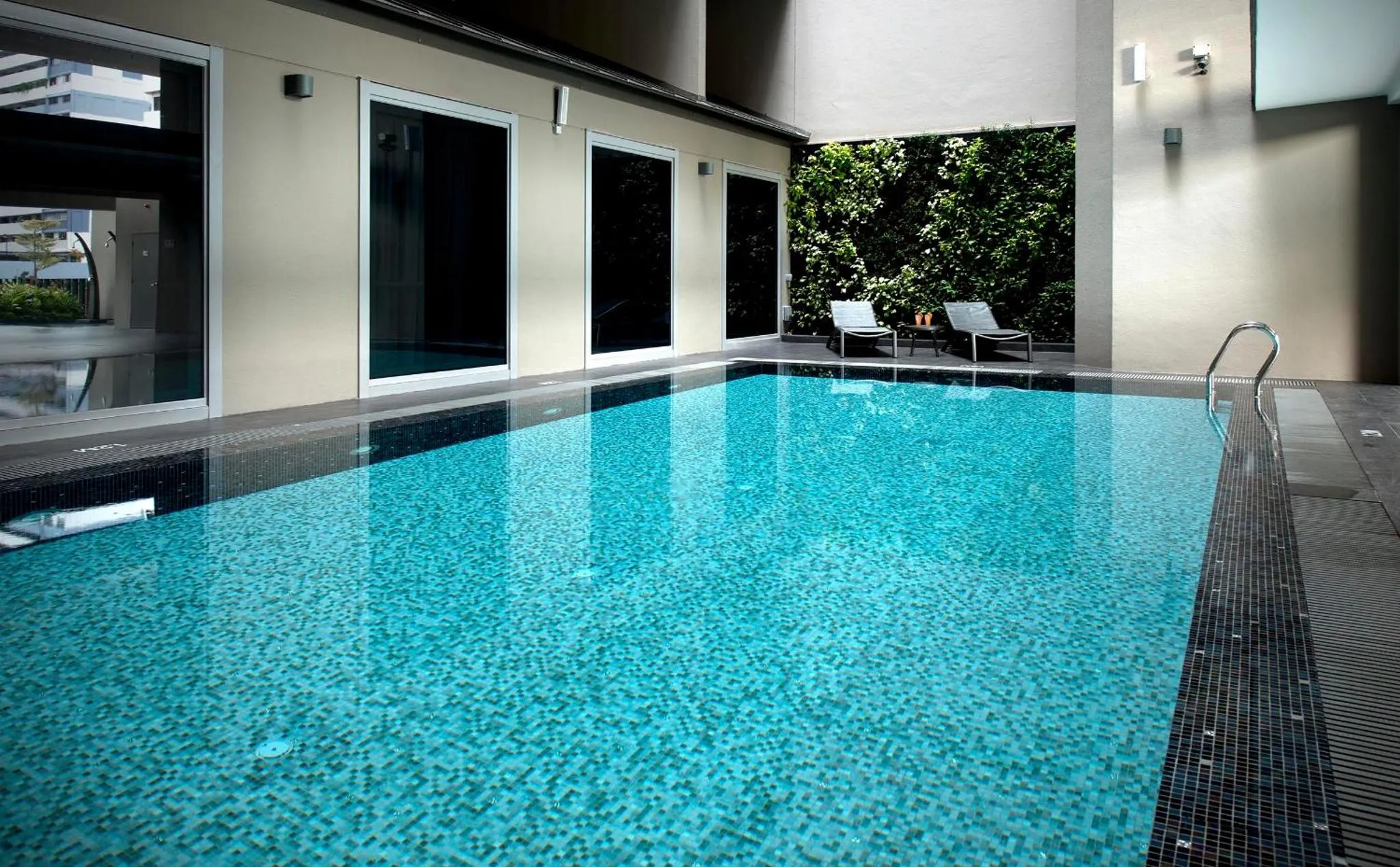 Une piscine rectangulaire turquoise avec deux chaises longues sur le bord.
