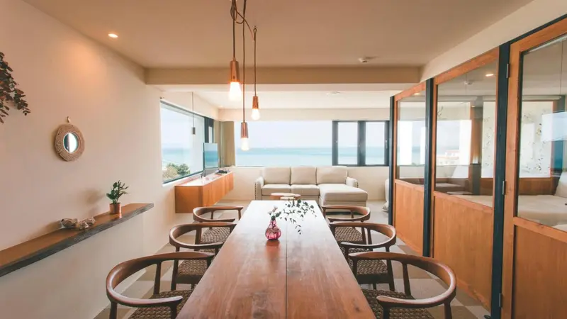 Une salle à manger lumineuse avec une grande table en bois et un canapé beige.