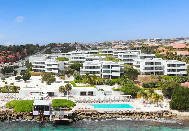 Vue aérienne d'un complexe hôtelier blanc avec piscine et accès à la mer.
