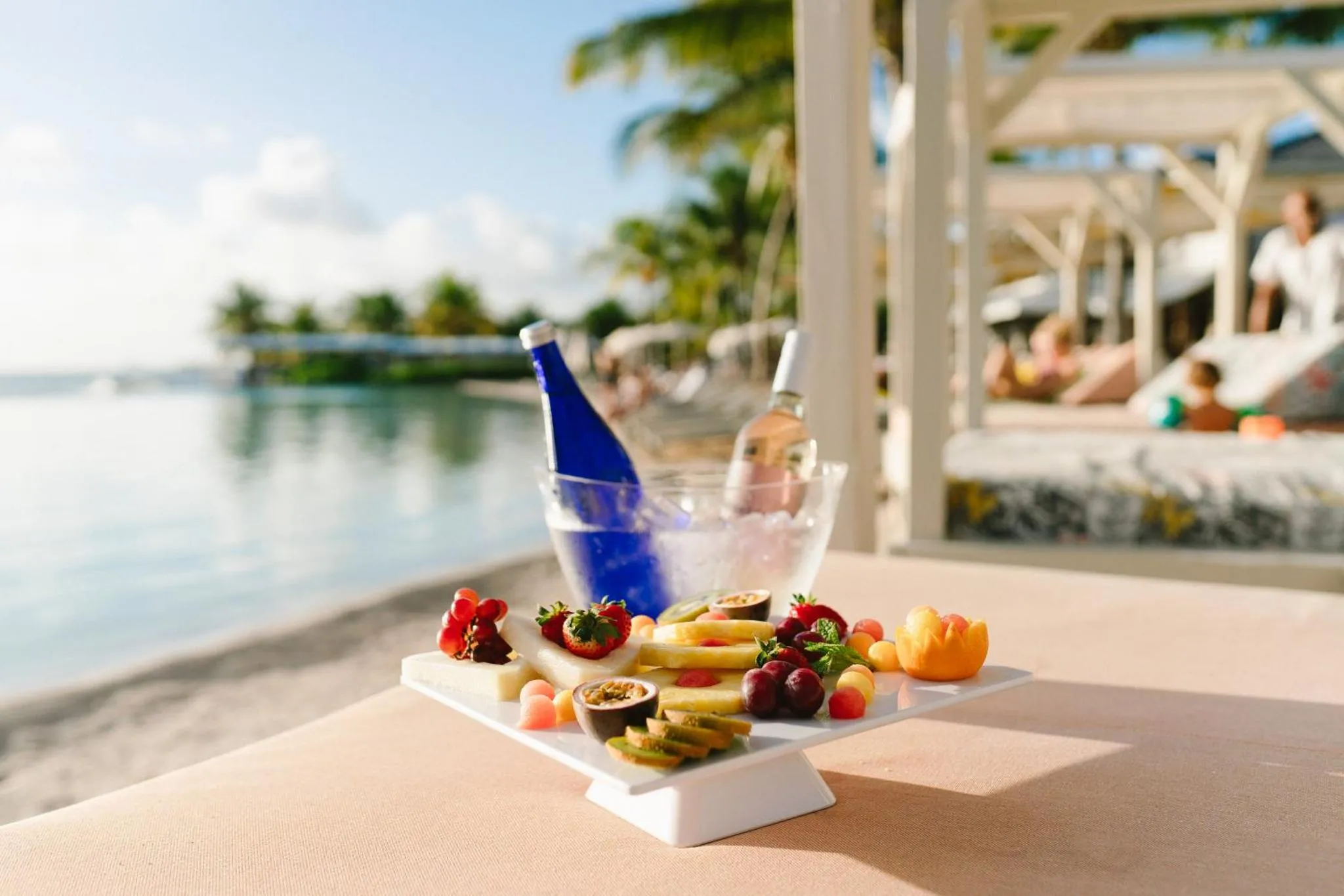 Une table présente une sélection de fruits frais et de boissons glacées sur une plage.