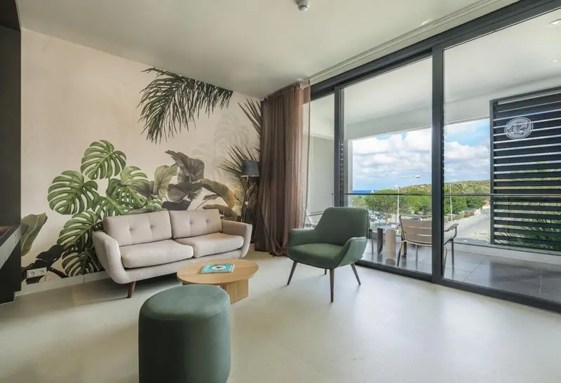 Un salon clair avec canapé et fauteuils, donnant sur une terrasse.