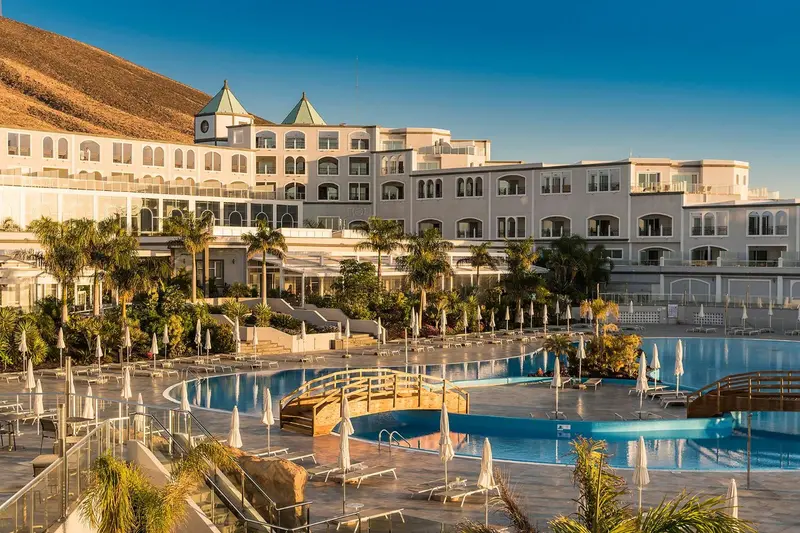 Vue d'un complexe hôtelier blanc avec des piscines et une végétation luxuriante.