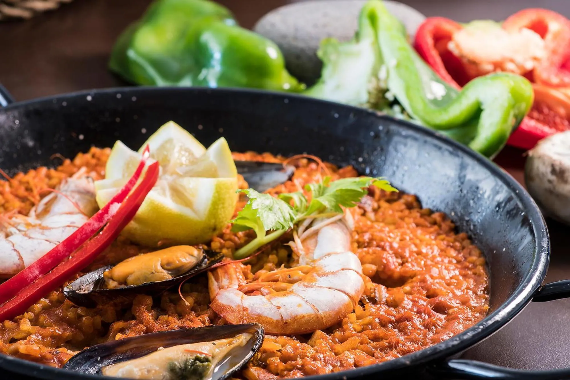 Une paella généreuse, ornée de fruits de mer et de légumes, est présentée dans une poêle noire.