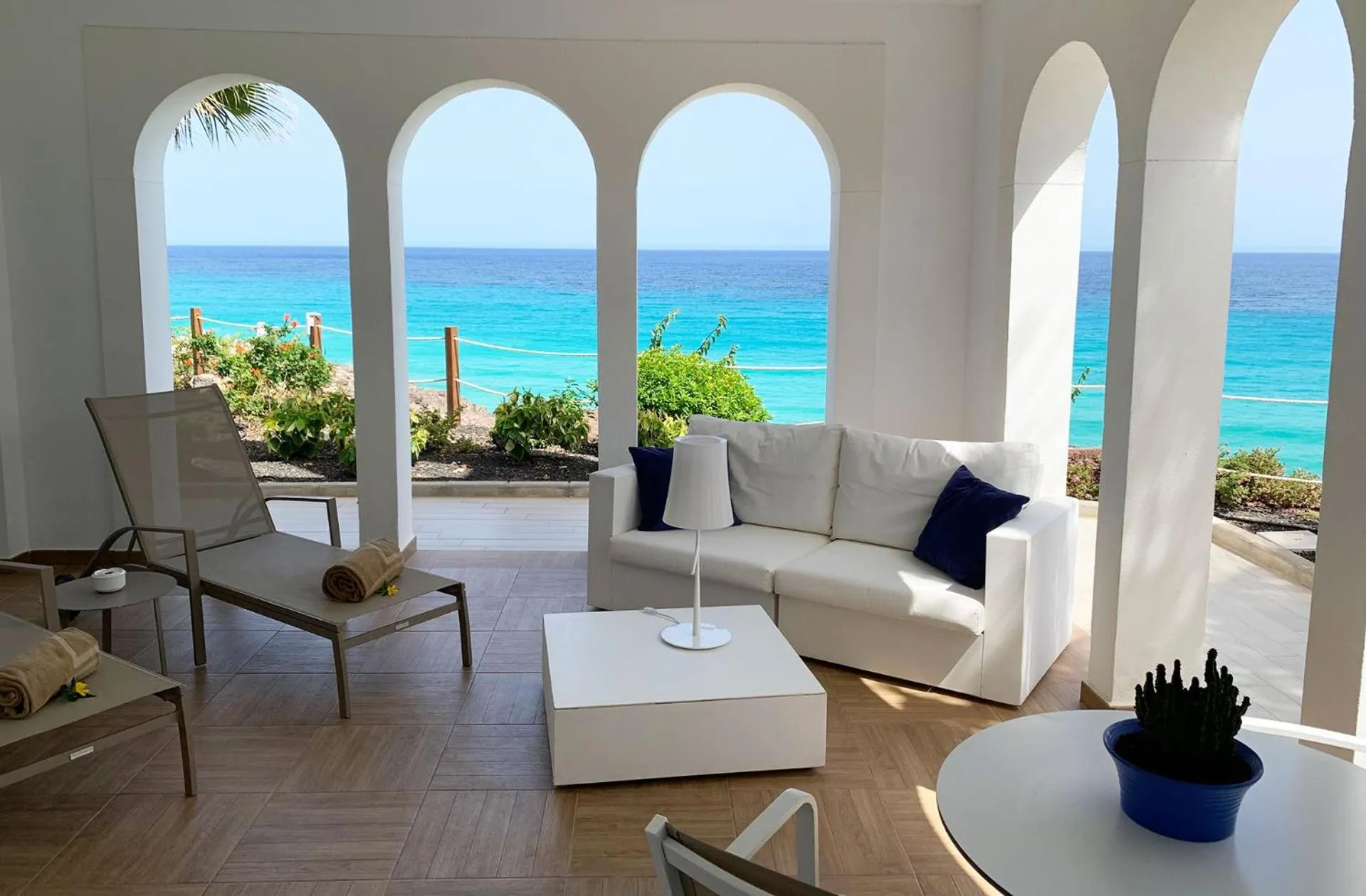 Espace de détente lumineux avec canapé blanc et vue sur la mer turquoise.