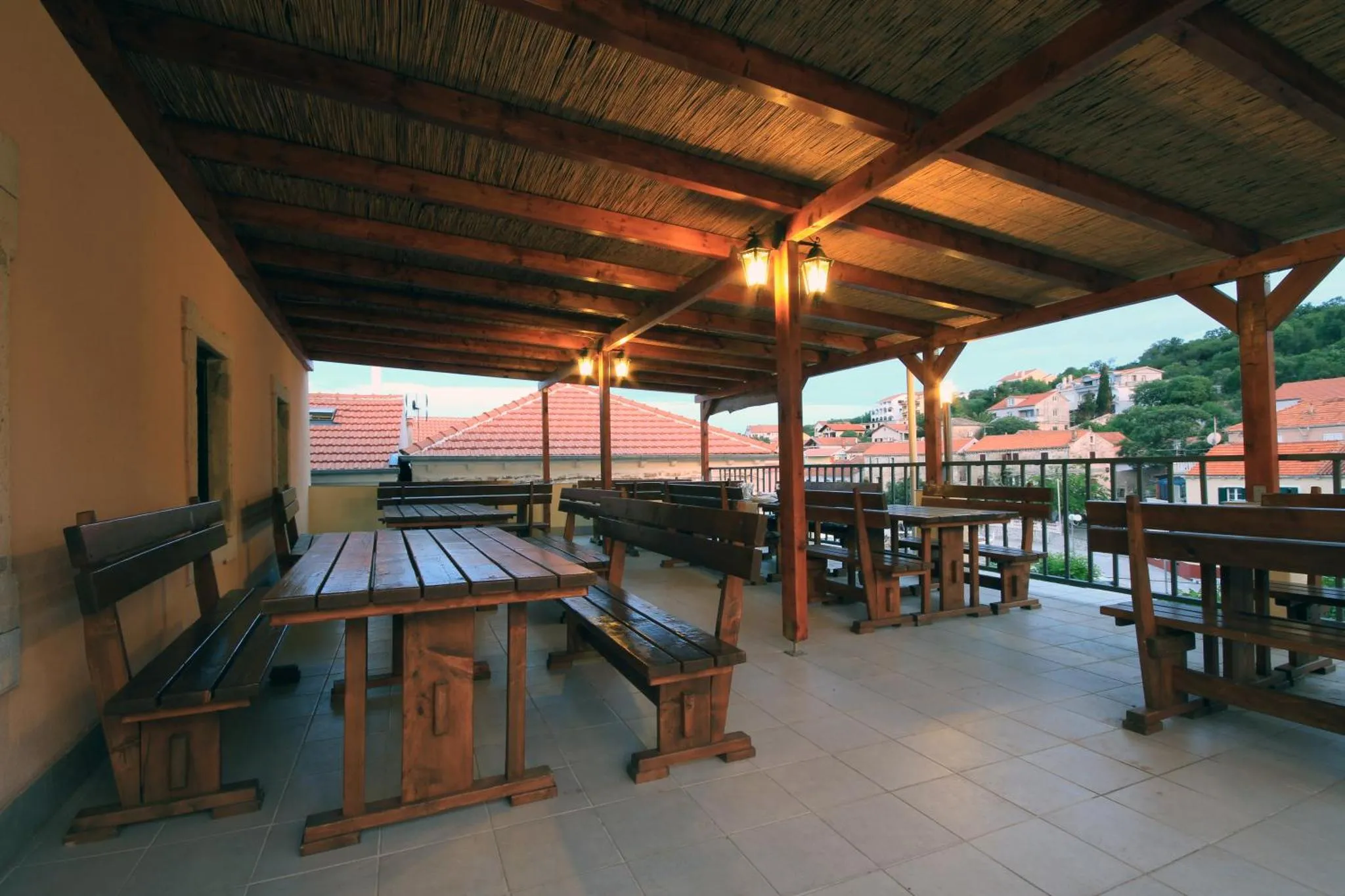 Terrasse ombragée avec tables et bancs en bois, vue sur un village.