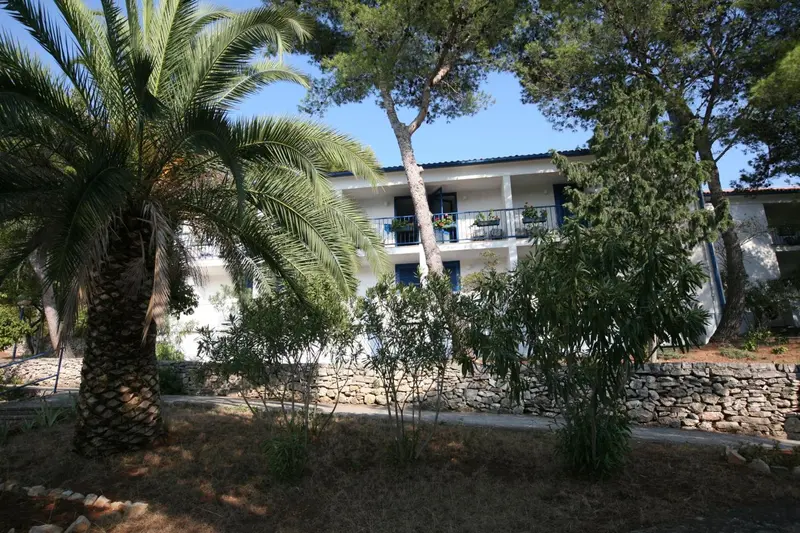 Bâtiment blanc à balcons entouré de végétation luxuriante et d'un jardin soigné.