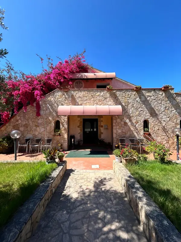 Façade d'un bâtiment avec une entrée ombragée et des bougainvilliers en fleurs.