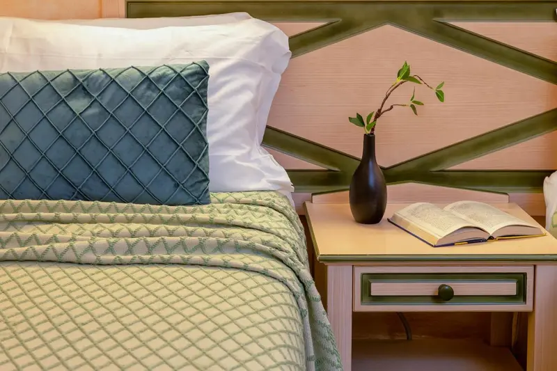 Un lit avec des oreillers et une table de chevet ornée d'un livre et d'une plante.