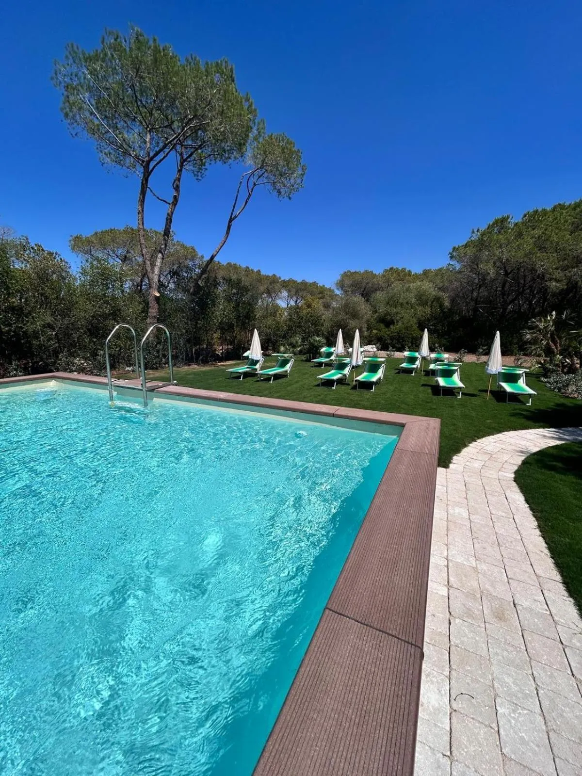 Une piscine rectangulaire turquoise bordée d'une pelouse verte et de transats.