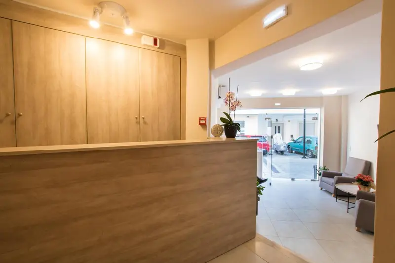 Un comptoir d'accueil moderne s'ouvre sur un espace lumineux avec des fauteuils et un parking.