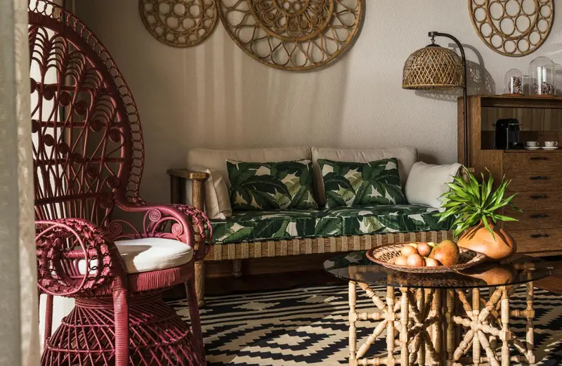 Un canapé et un fauteuil en rotin dans une pièce décorée de motifs végétaux.