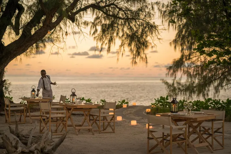Une table de restaurant est dressée sur une plage au coucher du soleil.