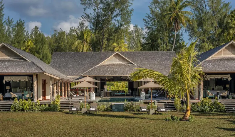 Bâtiments de style bungalow avec terrasse et piscine devant un jardin verdoyant.