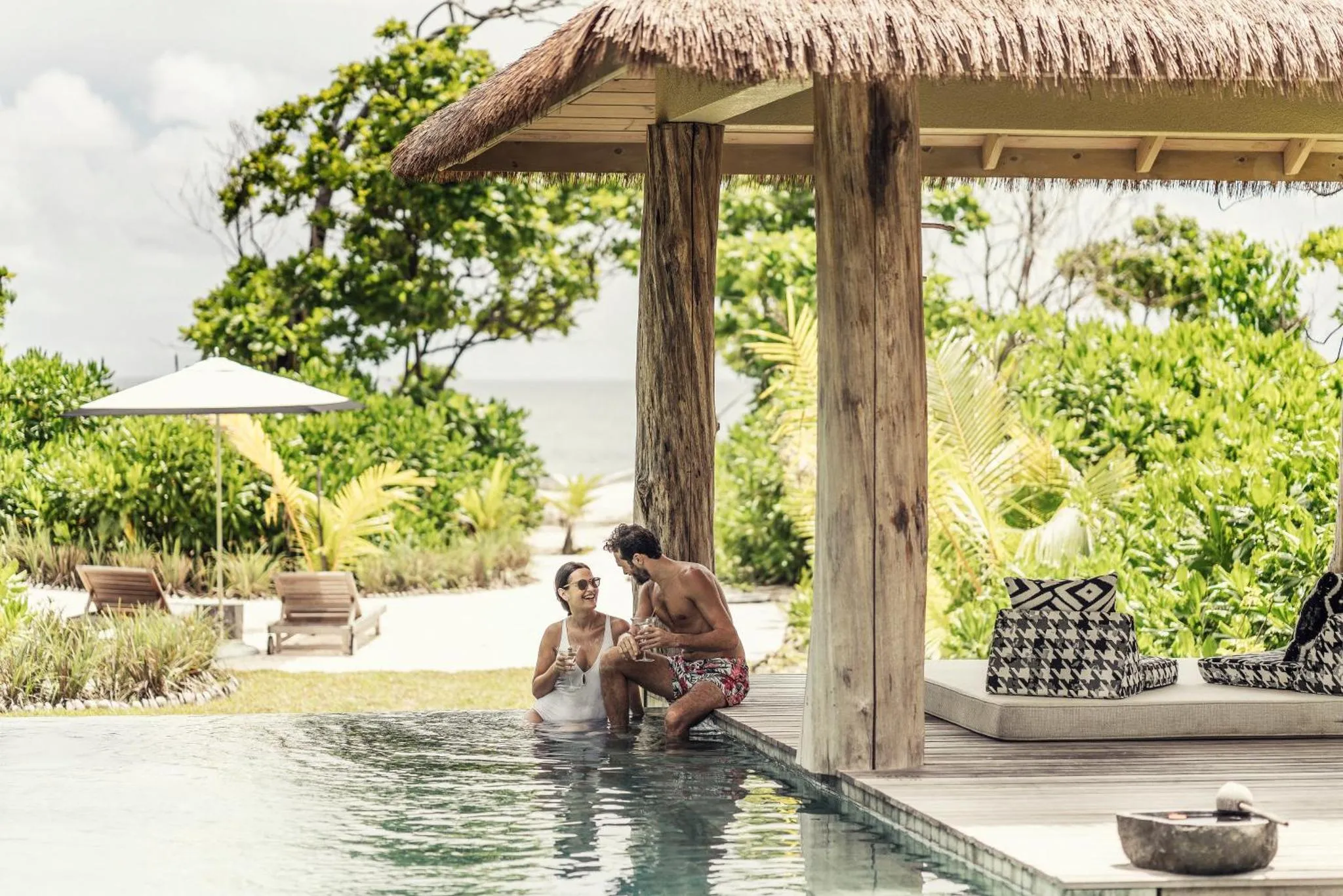 Un couple se détend au bord d'une piscine dans un cadre tropical.