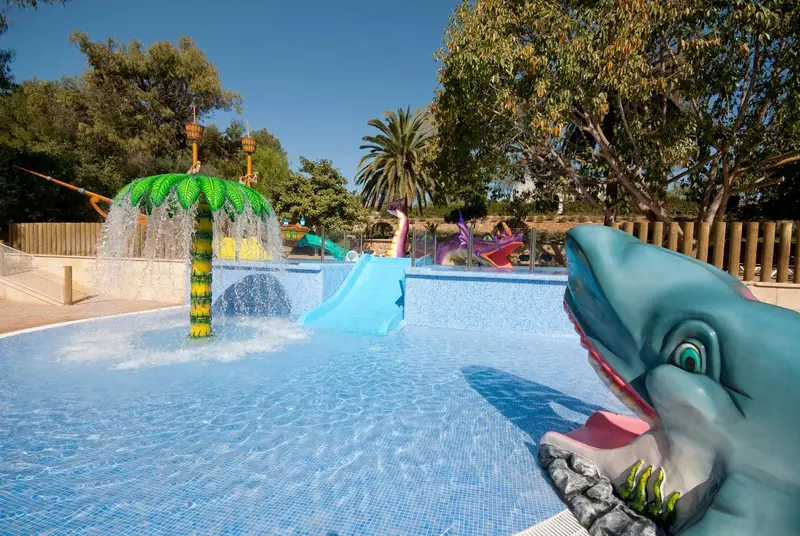 Une piscine avec des jeux d'eau et une structure en forme de requin.