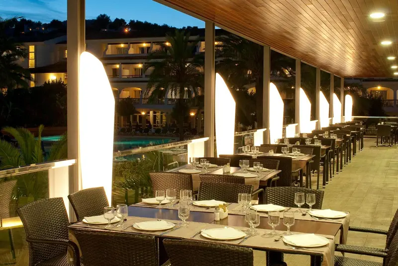 Tables dressées en terrasse avec une vue sur une piscine et des bâtiments éclairés.