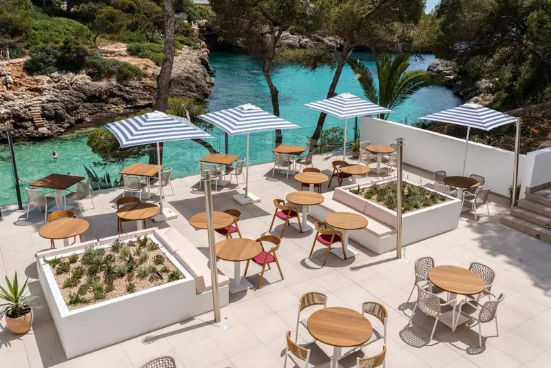 Terrasse aménagée avec tables et parasols au bord d'une crique turquoise.