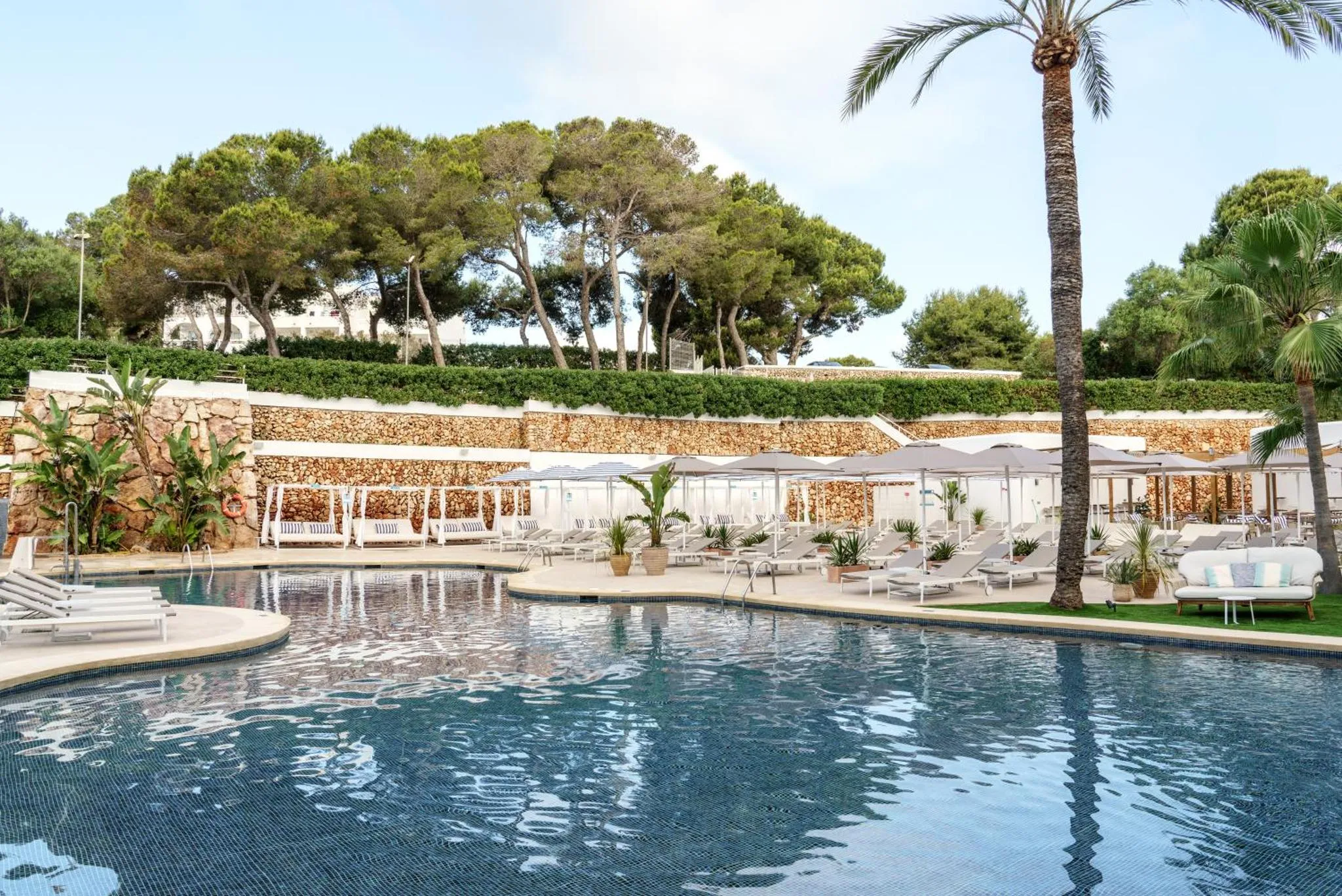 Transats blancs disposés autour d'une piscine bleue bordée de végétation.