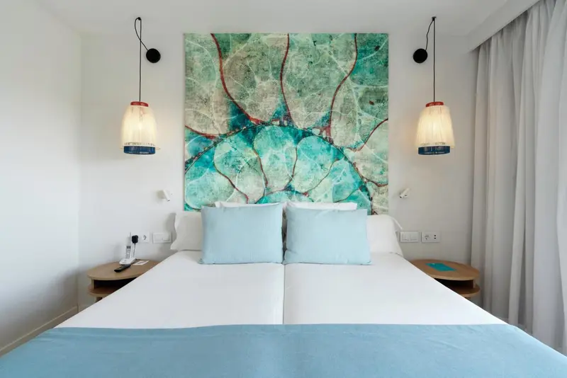Une chambre lumineuse avec un grand lit et une décoration murale abstraite.