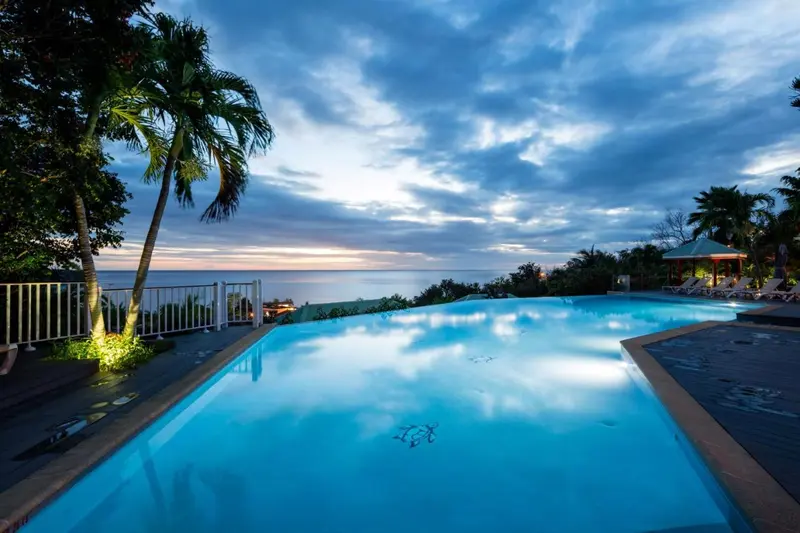 Une piscine à débordement illuminée surplombe la mer au crépuscule.