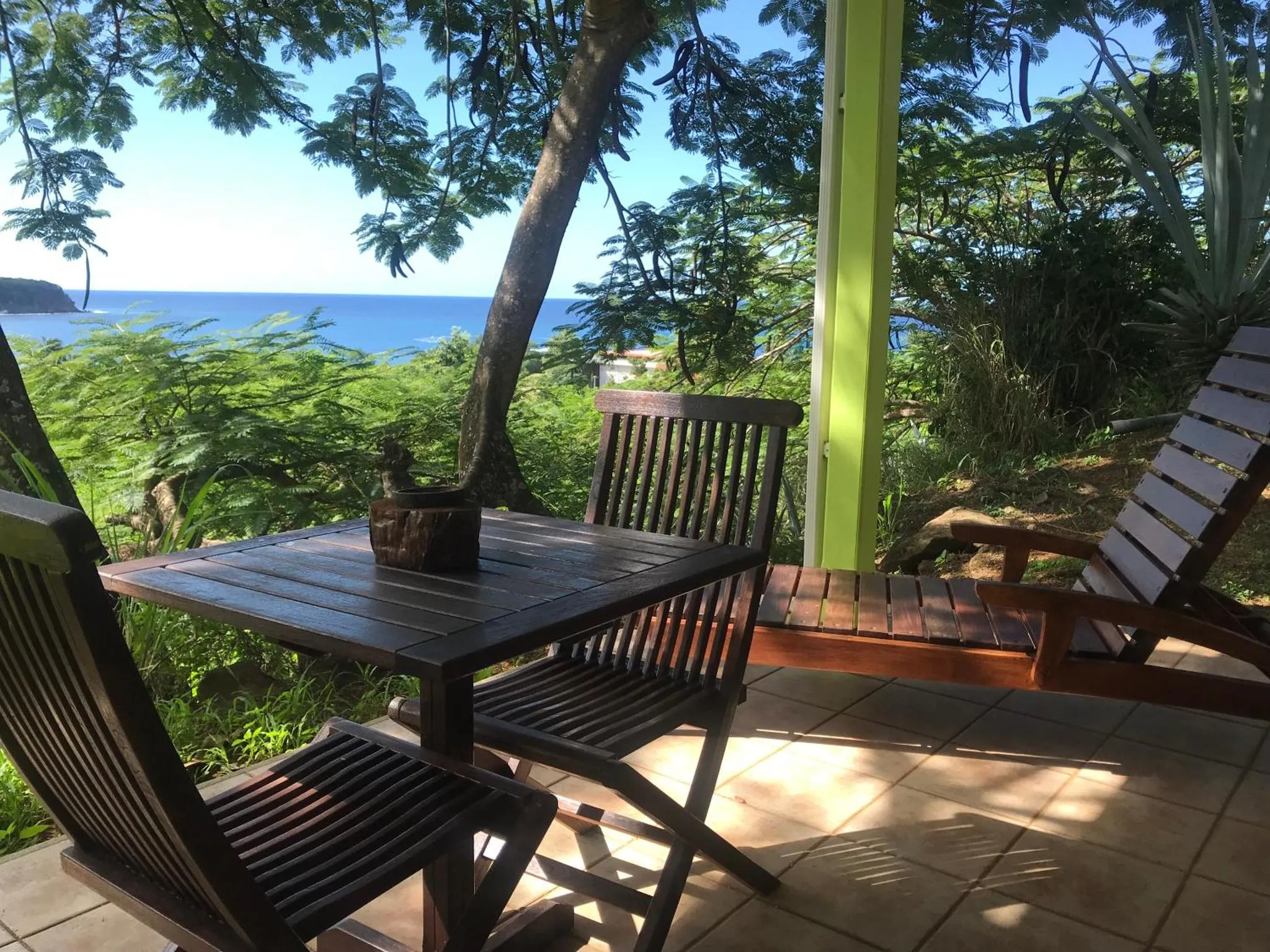 Une table et des chaises en bois invitent à la détente sur une terrasse ensoleillée avec vue sur la mer.