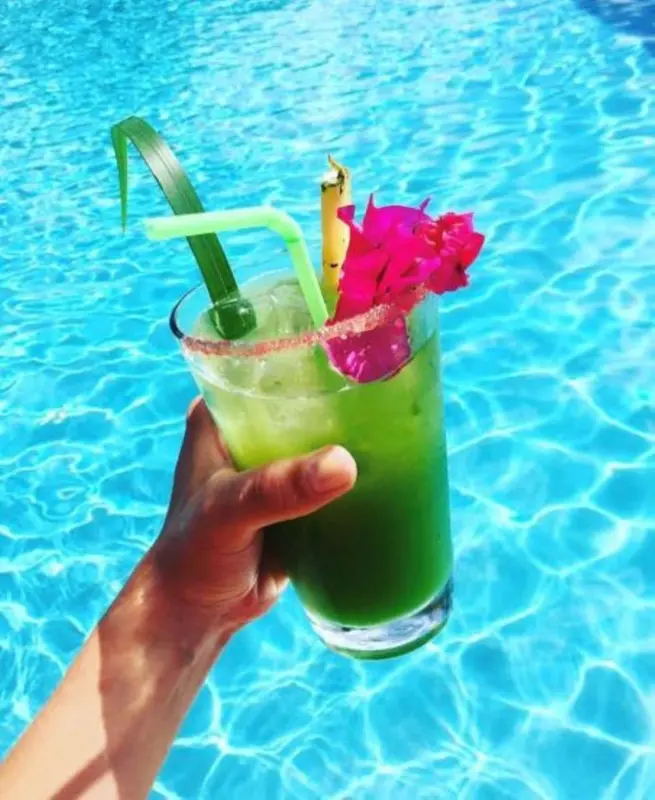 Un cocktail vert est tenu au-dessus d'une piscine scintillante.
