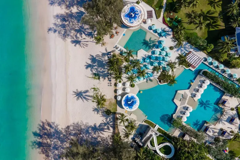 Vue aérienne d'une plage bordée de palmiers et d'une piscine sinueuse.