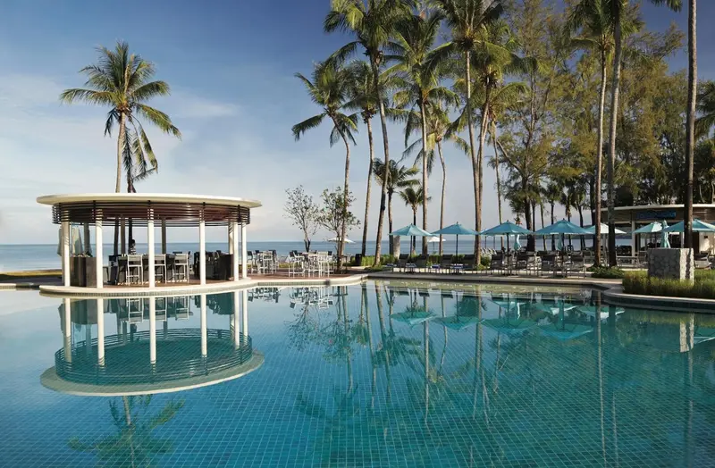 Une piscine turquoise reflète un ciel bleu et des palmiers.