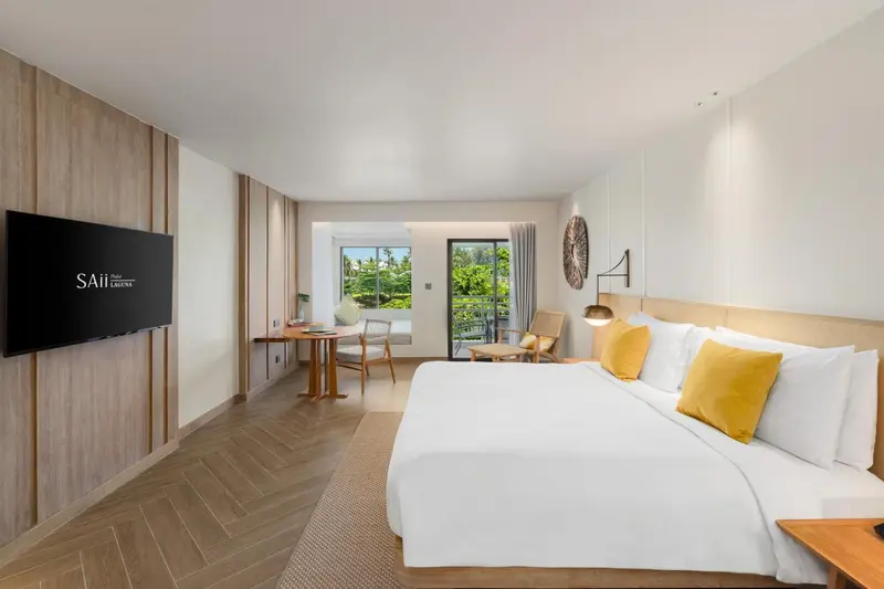 Chambre lumineuse avec un grand lit et un balcon donnant sur la végétation.