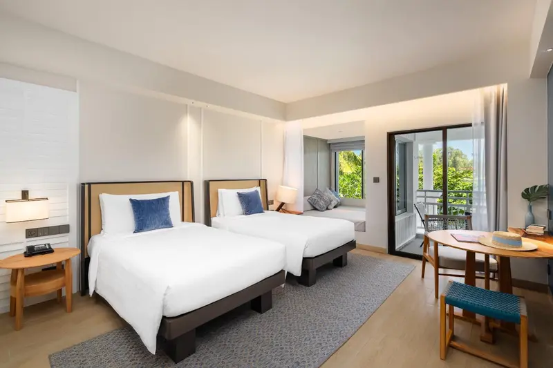 Chambre lumineuse avec deux lits simples et une table ronde près d'une baie vitrée.